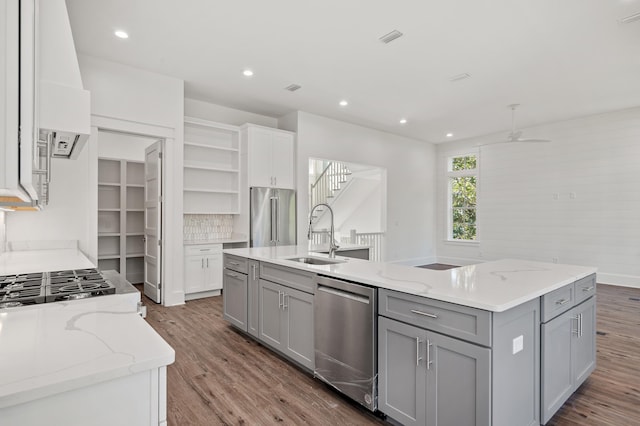 kitchen featuring gray cabinetry, sink, light stone countertops, an island with sink, and stainless steel appliances