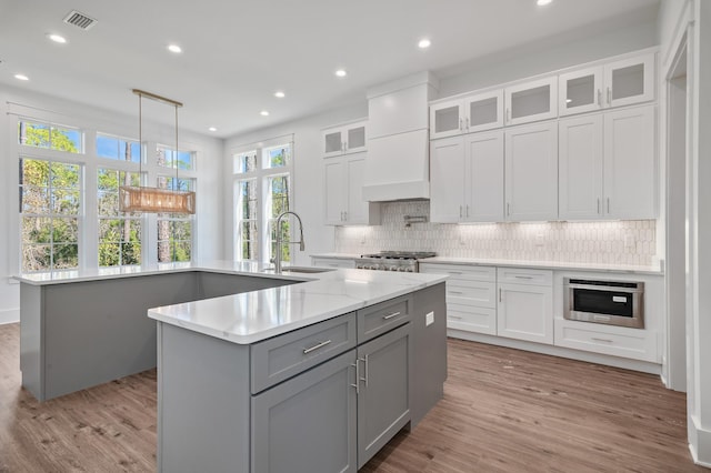 kitchen featuring gray cabinetry, hanging light fixtures, an island with sink, light hardwood / wood-style floors, and white cabinets