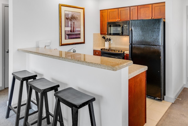 kitchen with kitchen peninsula, a kitchen bar, decorative backsplash, light tile patterned flooring, and black appliances