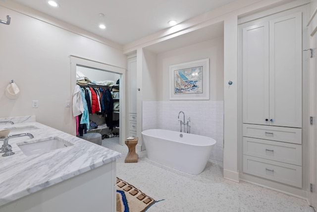 full bath featuring a freestanding bath, double vanity, wainscoting, tile walls, and a sink