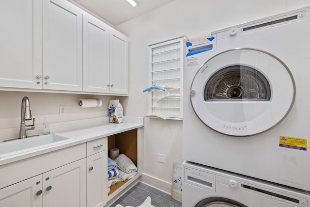 clothes washing area featuring cabinet space, stacked washer and clothes dryer, baseboards, and a sink