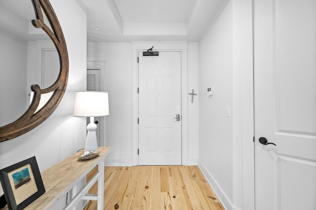 doorway to outside featuring baseboards, a raised ceiling, and light wood finished floors