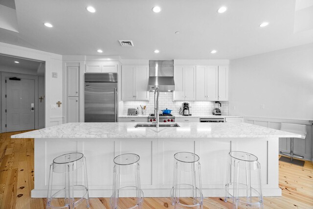 kitchen with visible vents, a large island with sink, stainless steel built in fridge, white cabinets, and wall chimney exhaust hood