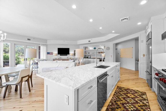 kitchen with visible vents, a center island with sink, a sink, light wood finished floors, and high end appliances