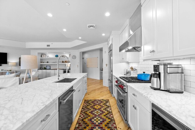 kitchen featuring visible vents, a sink, wall chimney exhaust hood, light wood finished floors, and high end appliances