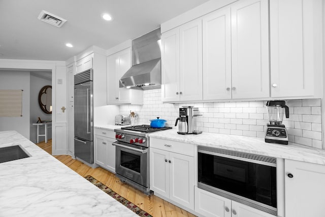 37 S Compass Point Way Unit 107, Inlet Beach, FL 32461 - kitchen with high quality appliances, wall chimney exhaust hood, light wood-type flooring, backsplash, and light stone countertops