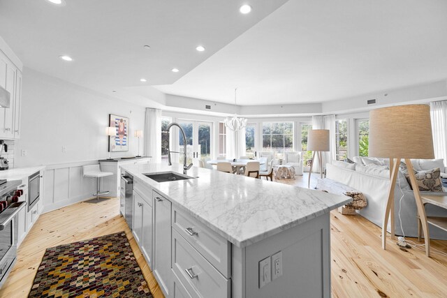 kitchen featuring a kitchen island with sink, a sink, light wood-style floors, appliances with stainless steel finishes, and open floor plan