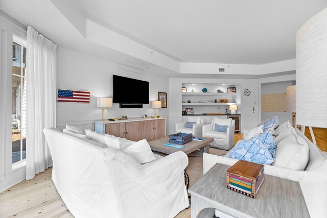 living room featuring a tray ceiling, built in shelves, and light wood-style floors