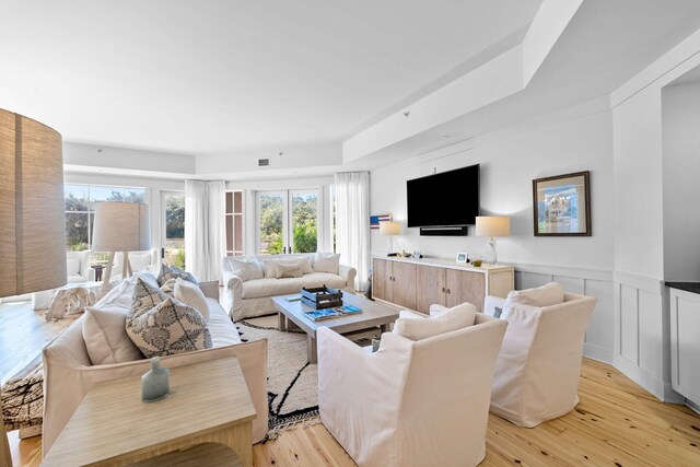 living area featuring a wainscoted wall, a healthy amount of sunlight, light wood-style flooring, and visible vents