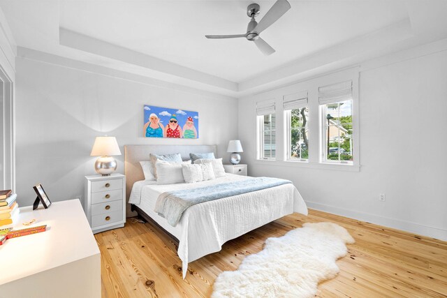 bedroom with light wood-type flooring, a tray ceiling, baseboards, and ceiling fan