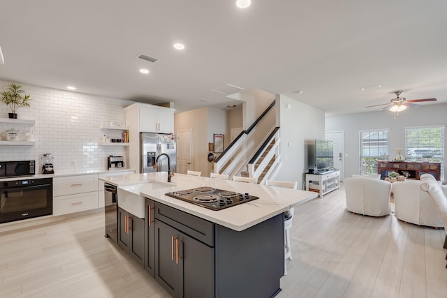 kitchen with white cabinetry, sink, backsplash, an island with sink, and black appliances