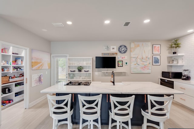 kitchen featuring white cabinets, light hardwood / wood-style floors, light stone countertops, and a kitchen island with sink