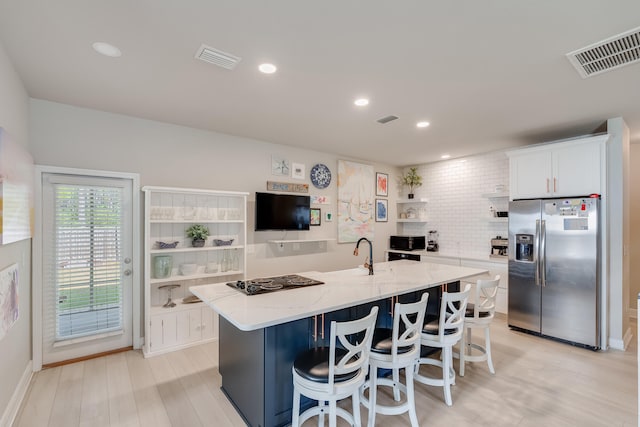 kitchen featuring light stone countertops, stainless steel fridge, a kitchen bar, and white cabinetry