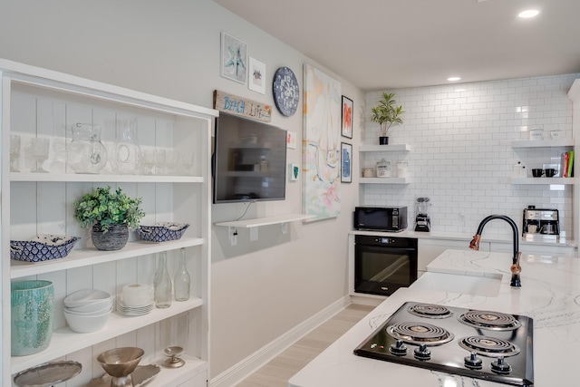 kitchen featuring sink, light stone counters, backsplash, light hardwood / wood-style floors, and black appliances