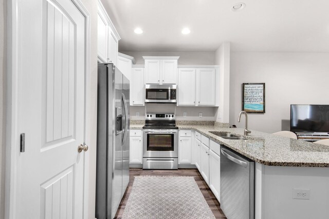 kitchen with dark hardwood / wood-style flooring, appliances with stainless steel finishes, white cabinets, kitchen peninsula, and sink