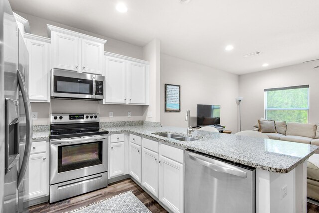 kitchen with appliances with stainless steel finishes, white cabinets, dark hardwood / wood-style floors, kitchen peninsula, and sink