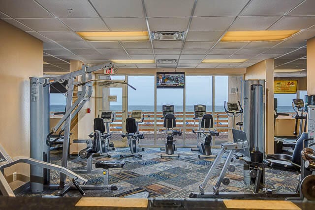 workout area with expansive windows, a paneled ceiling, and a water view