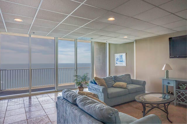 living room with tile floors, expansive windows, a water view, and a drop ceiling