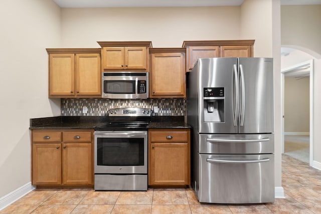 kitchen with light tile patterned flooring, dark stone countertops, appliances with stainless steel finishes, and tasteful backsplash