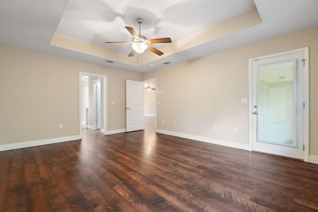 empty room featuring ceiling fan, dark wood-type flooring, and a tray ceiling