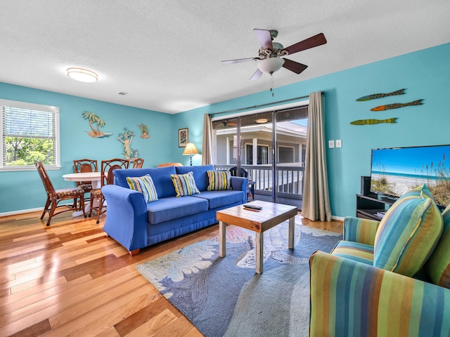 living room featuring ceiling fan, light hardwood / wood-style flooring, and a textured ceiling