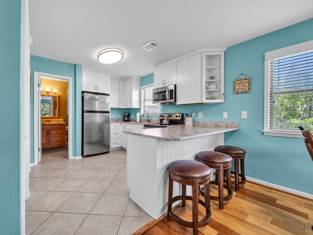 kitchen featuring white cabinets, a breakfast bar, stainless steel appliances, and kitchen peninsula