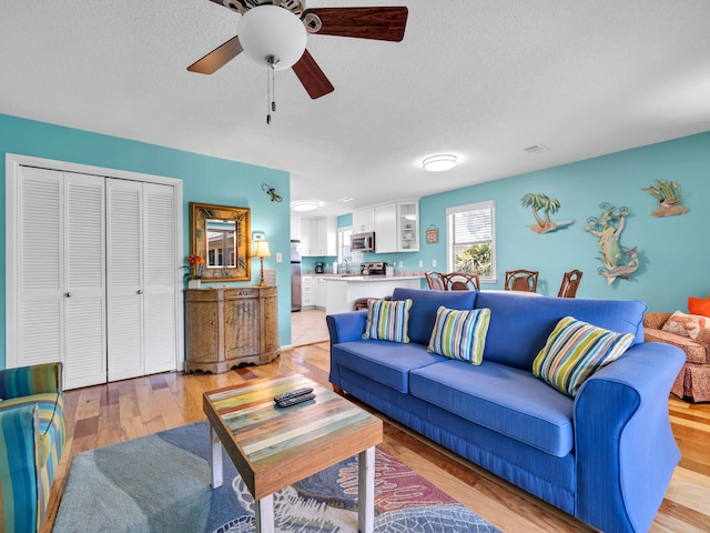 living room with ceiling fan, light hardwood / wood-style floors, and a textured ceiling