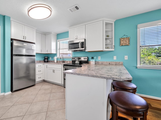 kitchen featuring kitchen peninsula, a breakfast bar, stainless steel appliances, light tile patterned floors, and white cabinetry