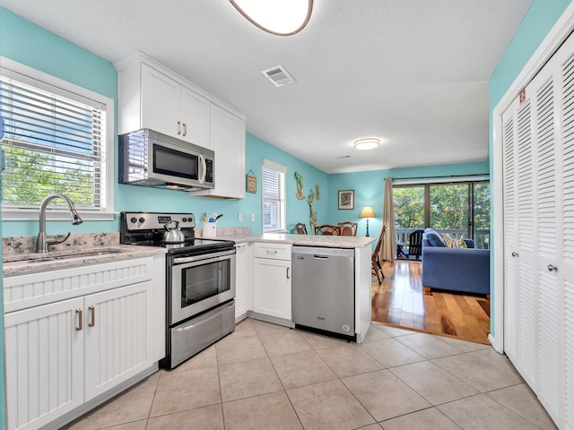 kitchen with sink, white cabinetry, light tile patterned flooring, kitchen peninsula, and stainless steel appliances