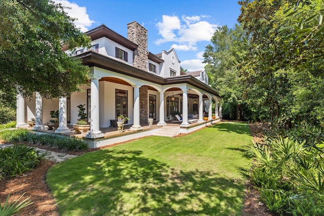 back of property with a chimney, a lawn, and stucco siding