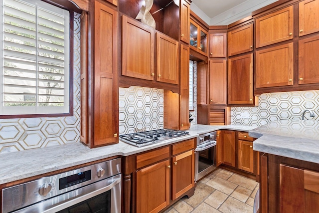 kitchen with brown cabinetry, stone tile floors, appliances with stainless steel finishes, and tasteful backsplash