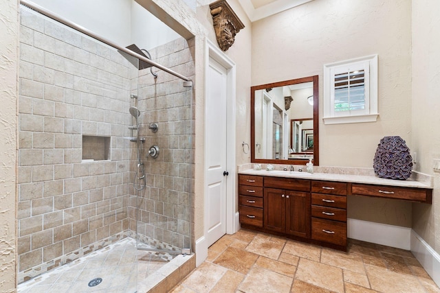 full bathroom featuring baseboards, a tile shower, stone tile flooring, and vanity