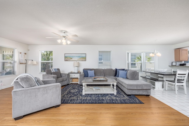 tiled living room featuring plenty of natural light, ceiling fan with notable chandelier, and a textured ceiling