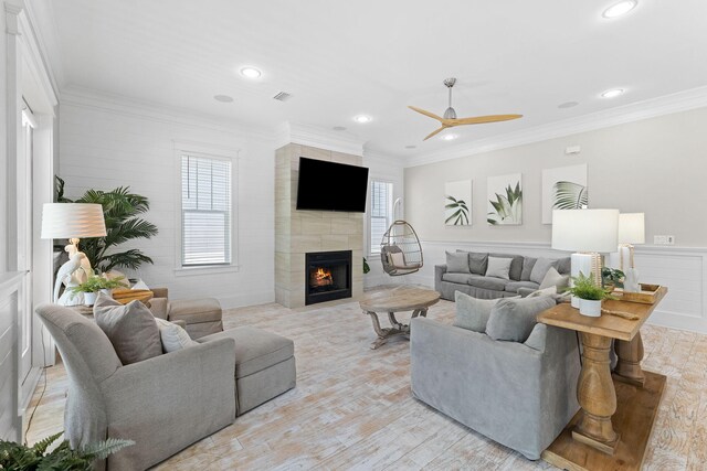 living room with a tiled fireplace, ornamental molding, ceiling fan, and light wood-type flooring