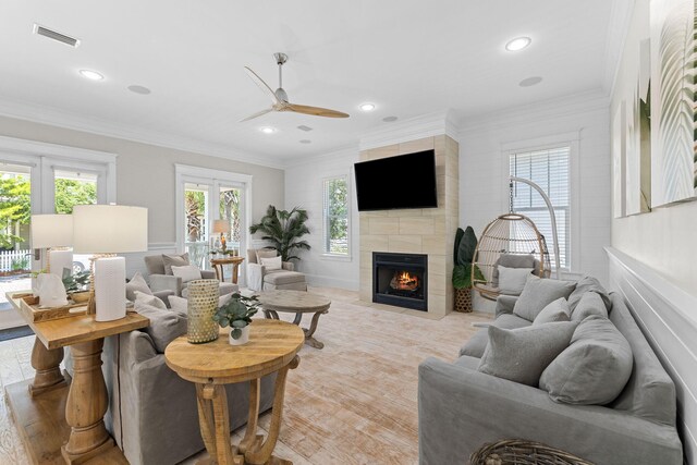 living room with a tiled fireplace, ornamental molding, and ceiling fan