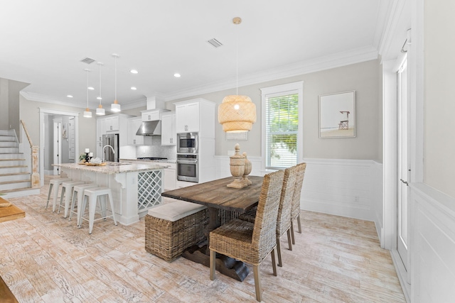 dining area with sink, ornamental molding, and light hardwood / wood-style floors