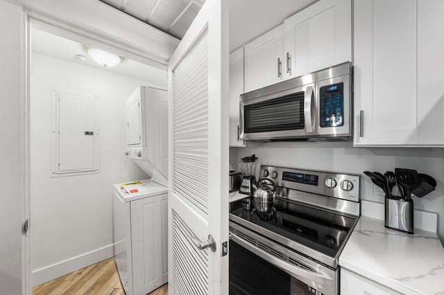 kitchen with light hardwood / wood-style floors, stainless steel appliances, stacked washer and clothes dryer, electric panel, and white cabinetry