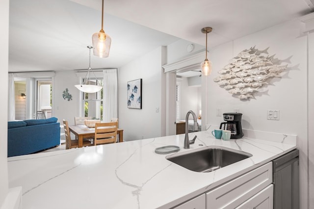 kitchen with pendant lighting, dishwashing machine, light stone countertops, and sink