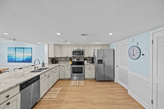 kitchen with sink, tasteful backsplash, light wood-type flooring, appliances with stainless steel finishes, and white cabinets