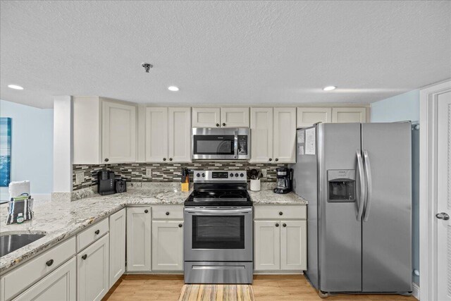 kitchen featuring tasteful backsplash, a textured ceiling, light wood-type flooring, appliances with stainless steel finishes, and light stone countertops
