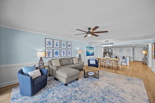 living room with ceiling fan, ornamental molding, light hardwood / wood-style flooring, and a textured ceiling