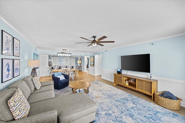 living room featuring hardwood / wood-style flooring, ornamental molding, ceiling fan with notable chandelier, and a textured ceiling