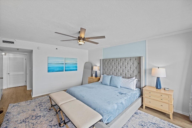 bedroom featuring ceiling fan, hardwood / wood-style flooring, ornamental molding, and a textured ceiling