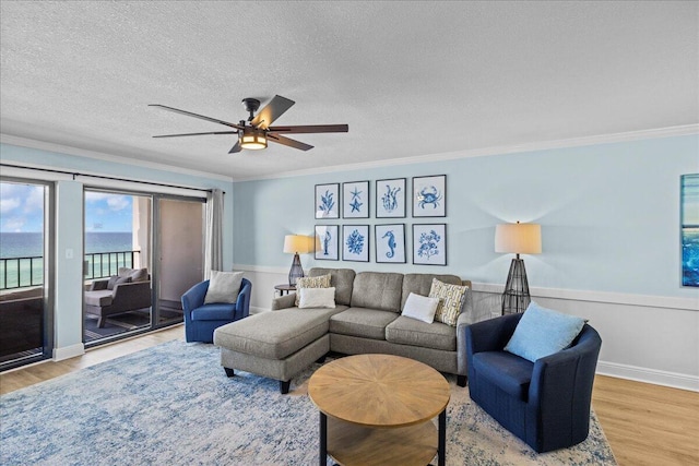 living room featuring hardwood / wood-style flooring, ornamental molding, ceiling fan, a water view, and a textured ceiling