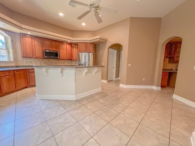 kitchen featuring ceiling fan, stainless steel appliances, a breakfast bar, light tile patterned flooring, and a center island with sink