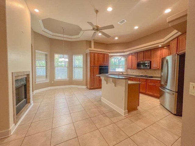 kitchen with ceiling fan, stainless steel appliances, a breakfast bar, light tile patterned floors, and a center island with sink