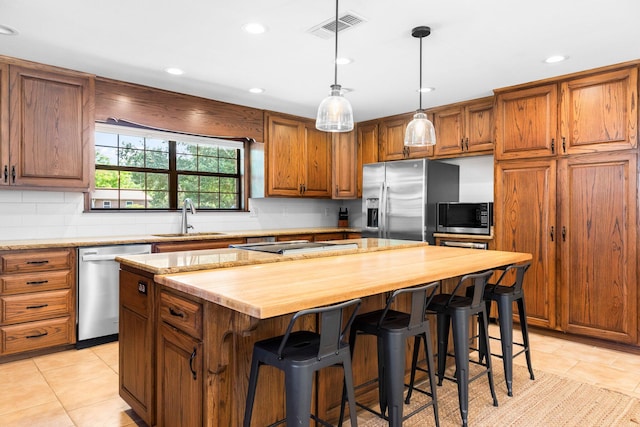 kitchen featuring a kitchen island, stainless steel appliances, a breakfast bar area, sink, and light tile floors