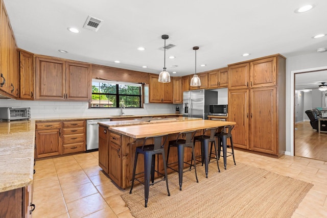 kitchen with stainless steel appliances, hanging light fixtures, a breakfast bar area, a center island, and light tile floors