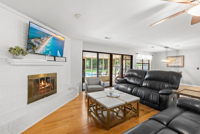 living room with brick wall, ceiling fan, light wood-type flooring, and a brick fireplace