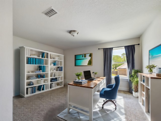 carpeted home office featuring a textured ceiling